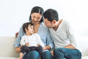 ソファに座る両親と幼児の家族。微笑み合いながらリラックスした様子。