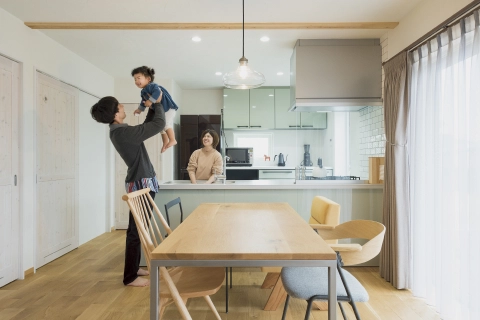 家族がダイニングキッチンで楽しく過ごす様子。父親が子供を抱き上げ、母親が微笑んでいる。